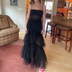 a woman standing in a living room wearing a black dress with sheer layers on it