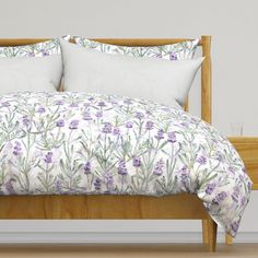 a bed with purple flowers on it and white pillows in front of the headboard