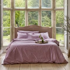 a bed with pink sheets and pillows in front of a large window that looks out onto the woods