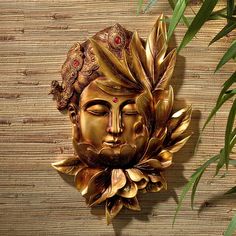 a golden mask is hanging on the wall next to a plant and bamboo leafy branches