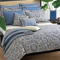 a bed covered in blue and white comforter next to a plant