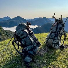 two backpacks sitting on top of a grass covered hill with mountains in the background