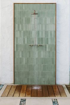 a green tiled shower in front of a white wall with wooden flooring and tile