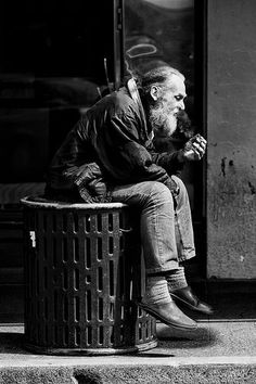 an old man sitting on top of a trash can next to a street sign that says, but love, full of rest