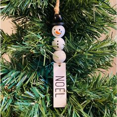 a snowman ornament hanging from a christmas tree with the word noel on it