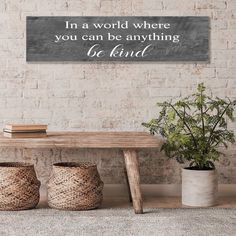 a wooden bench sitting in front of a brick wall with a sign above it that says, i'm a world where you can be anything be kind