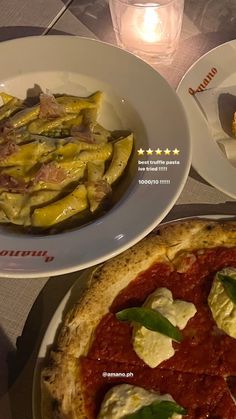 two plates with food on them sitting on a table next to a candle and some glasses