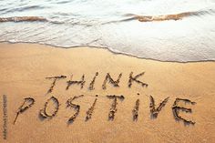 the words think positive are written in the sand