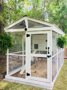 a white chicken coop in the middle of a yard with grass and trees around it