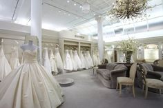 a room filled with lots of white dresses on mannequins and couches