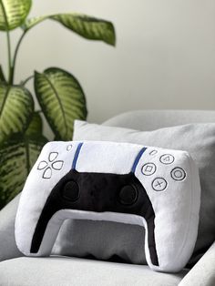 a pillow with a video game controller on it sitting on a couch next to a potted plant