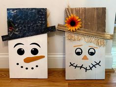 two snowmen made out of wooden boards on the floor with sunflowers in their hats