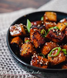 a black bowl filled with fried tofu and sesame seeds on top of a table