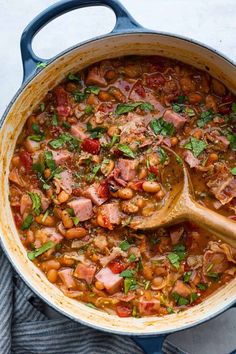 a pot filled with beans, ham and parsley on top of a wooden spoon