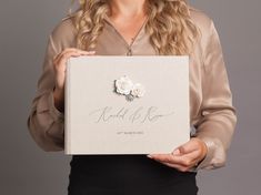 a woman holding up a wedding album with flowers on the front and back cover in her hands