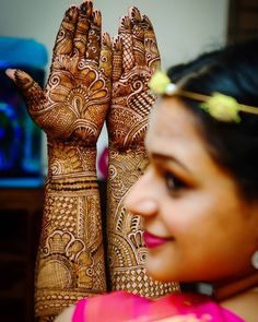 a woman holding her hands up to show the henna designs on her hand and face