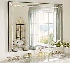 a bathroom sink with a large mirror above it and flowers on the counter in front of it