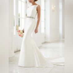 a woman in a white wedding dress standing next to a door and holding a bouquet