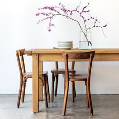 a wooden table topped with two chairs and a vase filled with flowers