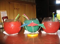 three glasses filled with liquid and straws sitting on top of a wooden table next to each other