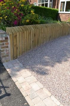 a wooden fence in front of a brick wall and flowerbeds on the side