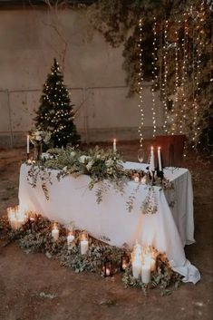 a table with candles and greenery on it in front of a lit christmas tree