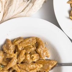 two white plates filled with pasta next to a bag of noodles and a fork on the table