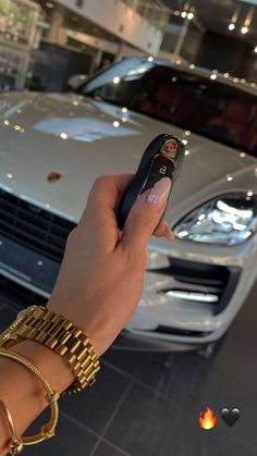 a hand holding a remote control in front of a white car with gold bracelets