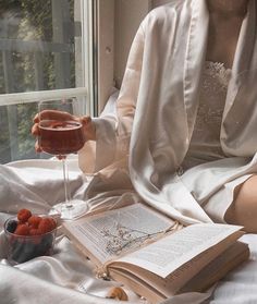 a woman sitting on a bed with a book and glass of wine in her hand