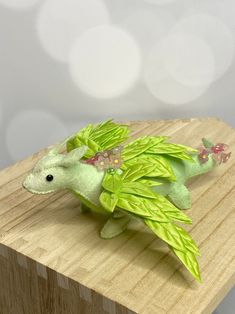 a small green stuffed animal sitting on top of a wooden table next to a white wall