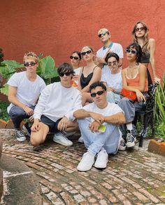 a group of young people sitting next to each other on a brick floor in front of a red wall