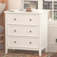 a white dresser with two drawers and a cup on top of it next to a bed