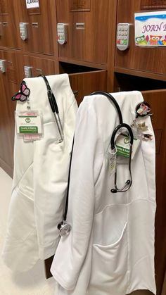 two medical coats hanging on the wall in a room with wooden cabinets and white flooring