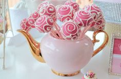 pink and white chocolate covered candies in a teapot shaped like a flower arrangement