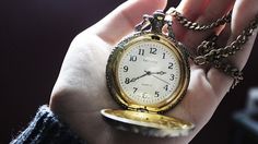 a person holding an antique pocket watch in their hand with chain around the clock face