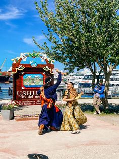 two people dancing in front of a sign with boats in the water behind them on a sunny day