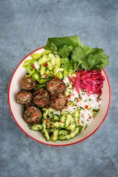 a bowl filled with meatballs, cucumbers and red cabbage sprouts