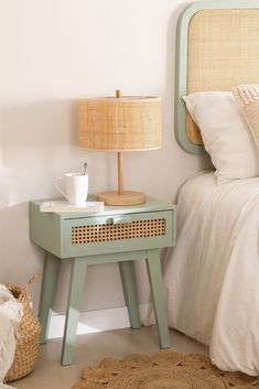 a small table with a cup on it next to a bed and a basket under the headboard