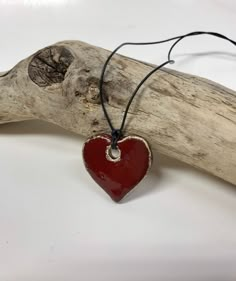 a red heart shaped pendant hangs from a piece of driftwood on a white background