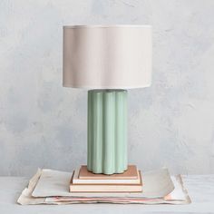 a green table lamp sitting on top of a stack of books next to a white lampshade