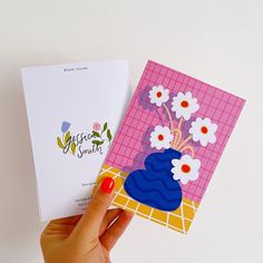 a hand holding two greeting cards with flowers in a blue vase on the front and pink checkered background