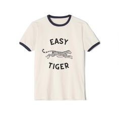 Easy Tiger Retro Ringer T-Shirt Embrace a playful yet classic vibe with our "Easy Tiger" retro ringer t-shirt. Featuring a vintage-inspired tiger graphic, this tee blends timeless style with a touch of whimsy, making it a standout piece for anyone who loves a good throwback and a fun twist. Features: Premium Fabric: Made from a high-quality blend of 100% Airlume combed and ring-spun cotton, this lightweight (4.2 oz/yd²) tee offers superior breathability and comfort. Perfect for layering or wearing solo, great for both active days and laid-back lounging. Classic Ringer Design: This retro ringer tee features contrasting ribbed collars and sleeve bands, enhancing its vintage appeal. The crew neckline and relaxed fit ensure a comfortable, classic look that never goes out of style. Durable Cons Tiger Graphic, Animal Graphic Tee, Classic Vibe, Entertaining Decor, Easy Tiger, Tiger Design, Time Kids, Animal Graphic, Ringer Tee