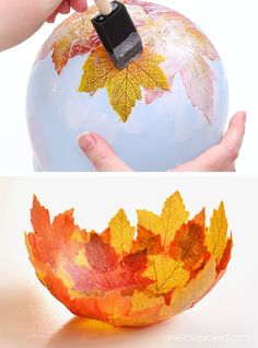 a hand holding a paintbrush over a painted globe with autumn leaves on the surface