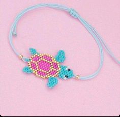 a pink and blue beaded turtle on a light blue cord with gold beads is sitting on a pink surface