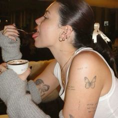 a woman with tattoos on her arm drinking from a cup