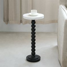 a white table with a black base and a cup on it next to a couch