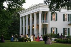 a group of people standing in front of a large white house