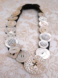 a close up of a necklace with buttons on a lace table cloth background and an ornate design