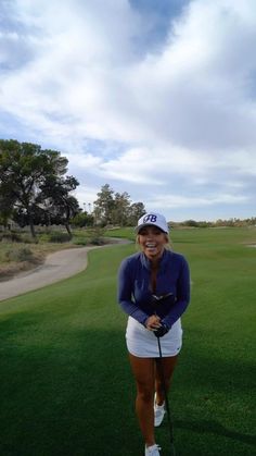 a woman standing on top of a lush green golf field holding a golf racquet