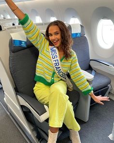 a woman is sitting on an airplane with her arms in the air and smiling at the camera